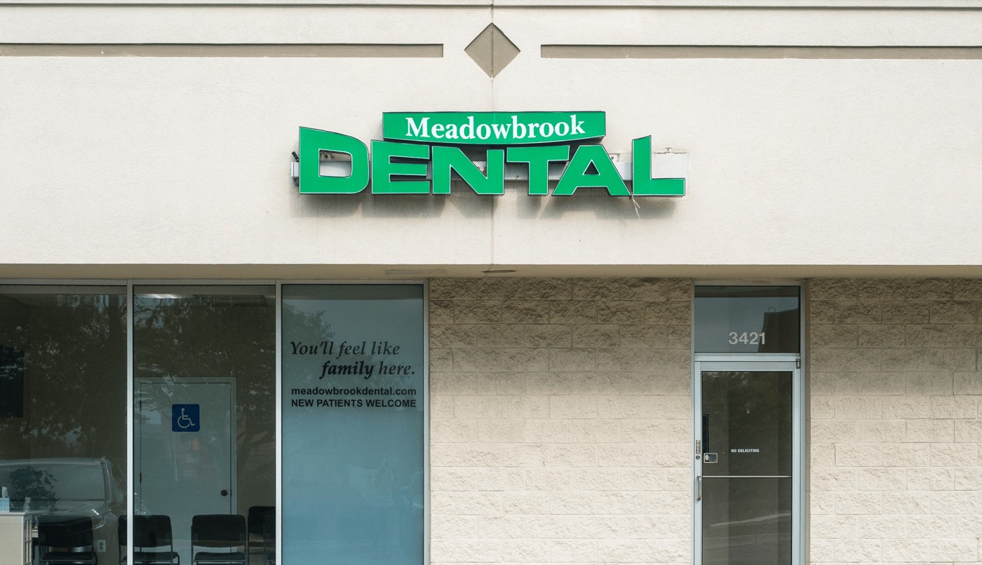 The Meadowbrook Dental storefront at 3421 Five Points Drive. The practice's green sign sits above the entrance, and the window reads "You'll feel like family here — new patients welcome".
